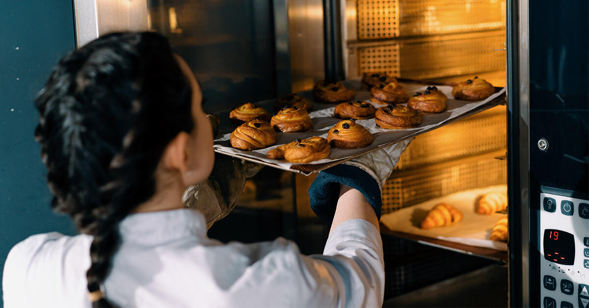 Kvinnelig kokk tar ut et brett med boller fra bake-off ovn